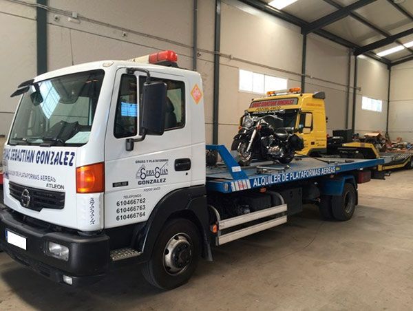 Una grúa con una motocicleta en la parte trasera está estacionada en un almacén.
