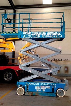 Un elevador de tijera azul está estacionado en un garaje al lado de un camión.