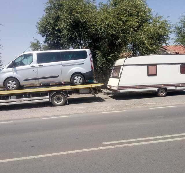 Una furgoneta está siendo remolcada por una grúa al lado de una caravana.