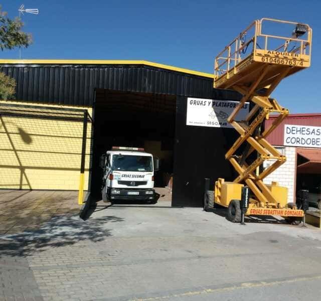Un elevador de tijera amarillo está estacionado frente a un edificio que dice Dehesas Cordone