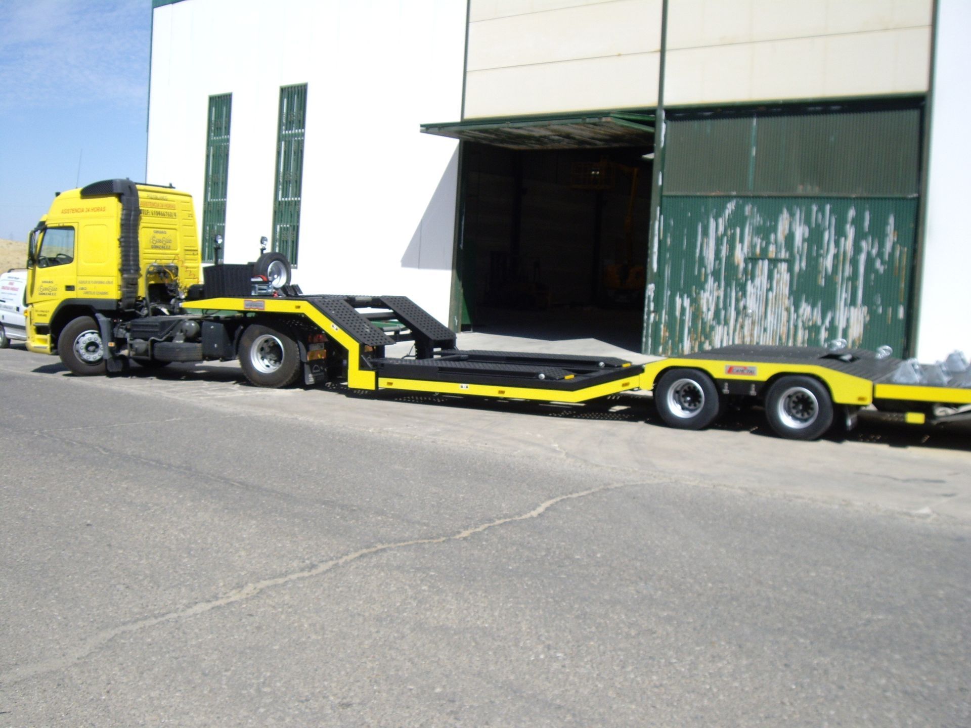 Un camión semirremolque amarillo está estacionado frente a un edificio.