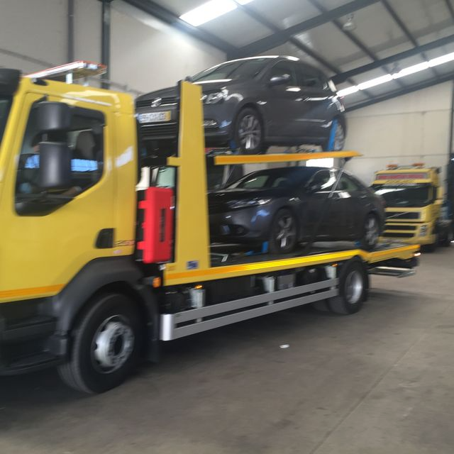 Una grúa amarilla con dos coches encima.