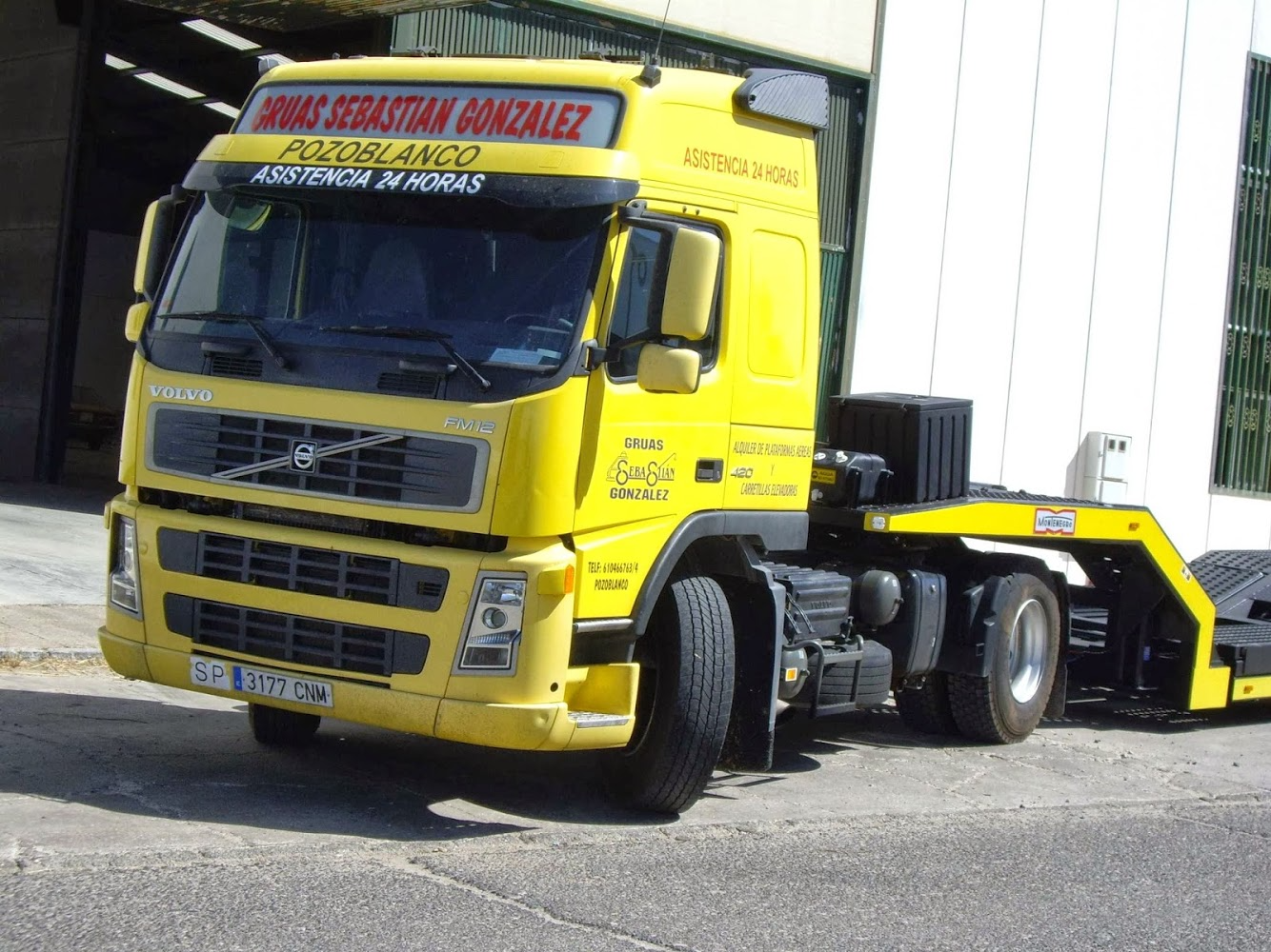 Un camión semirremolque Volvo amarillo está estacionado frente a un edificio.