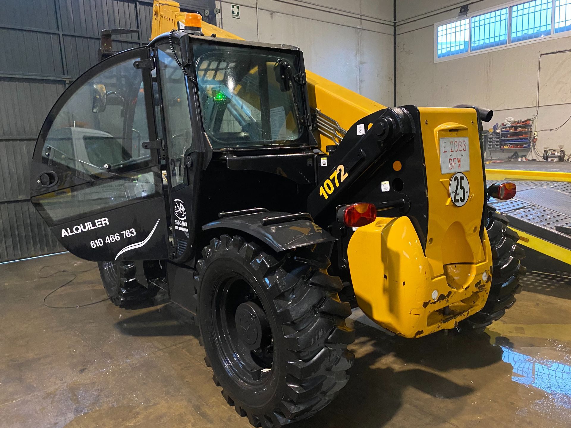 Un tractor amarillo y negro está estacionado en un garaje con las puertas abiertas.