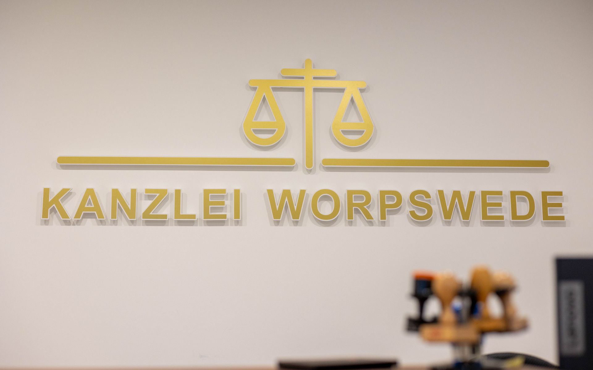 Ein Schild an einer Wand mit der Aufschrift „Kanzlei Worpswede“ und einer Waage der Gerechtigkeit darauf.