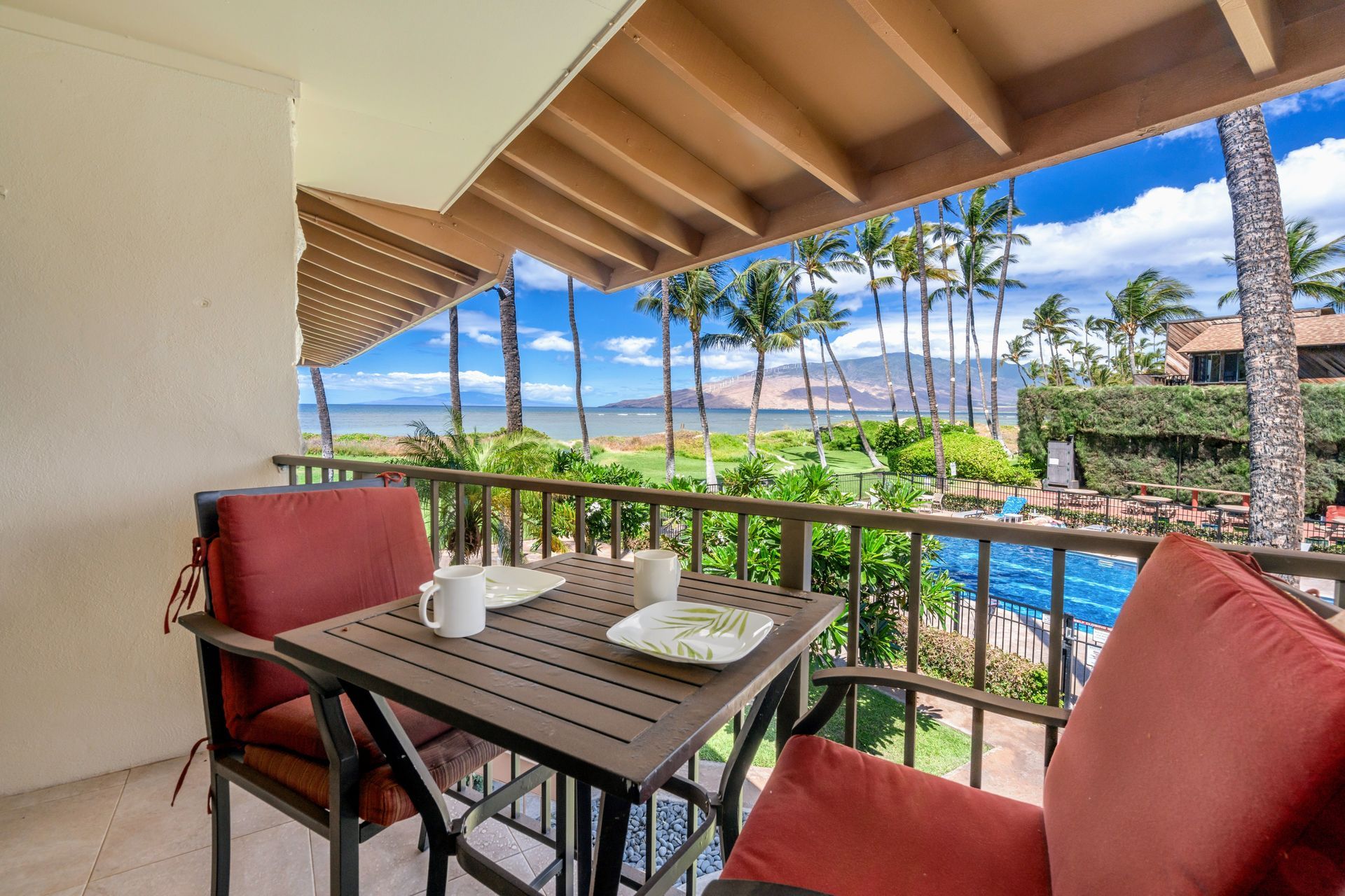 There is a table and chairs on the balcony with a view of the ocean.