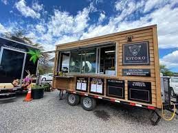 A food truck is parked in a gravel lot.