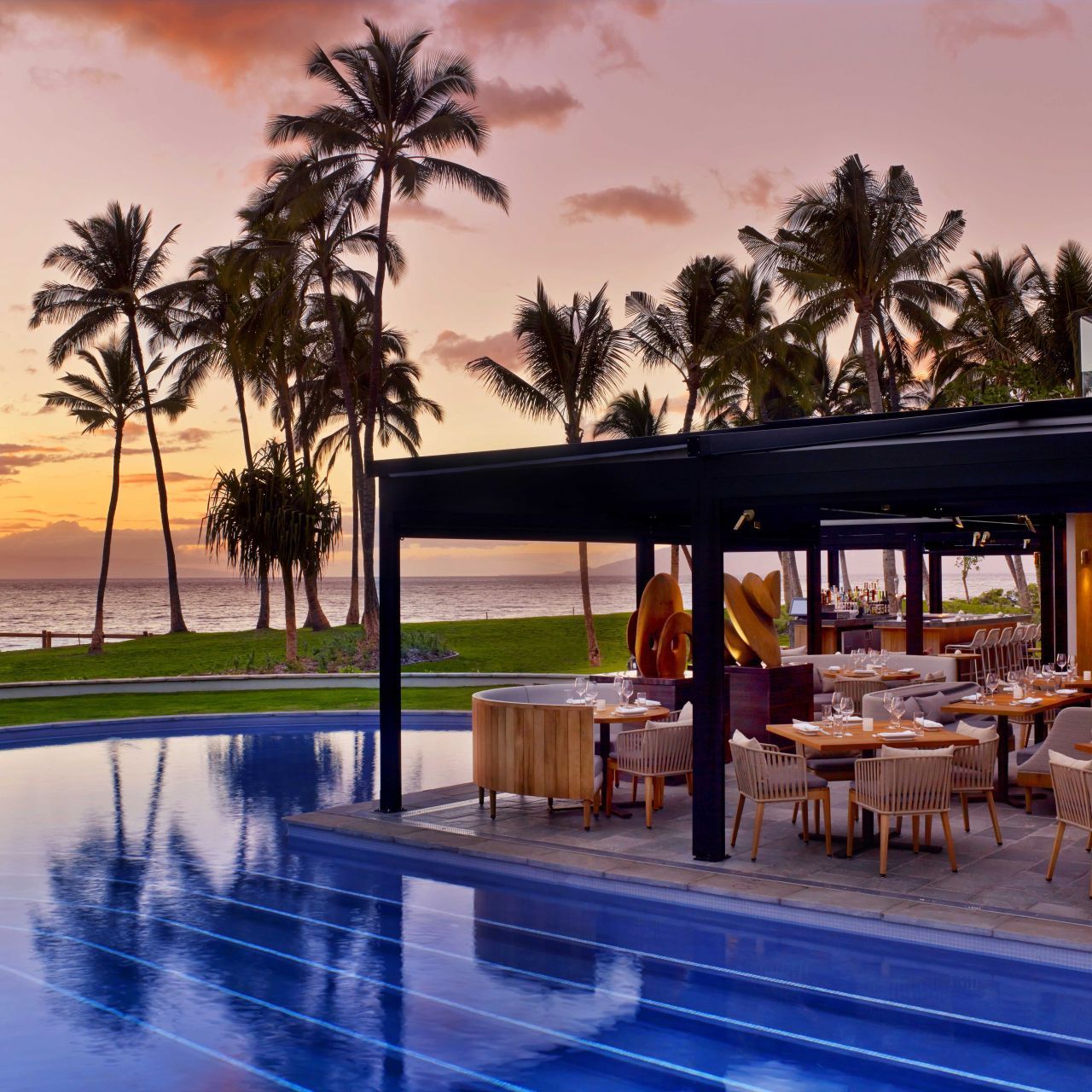A swimming pool surrounded by tables and chairs with palm trees in the background