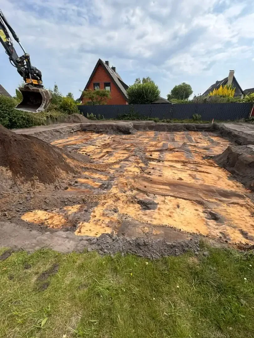 Ein gelber Bagger lädt Erde auf einer Baustelle in einen Muldenkipper, blauer Himmel.