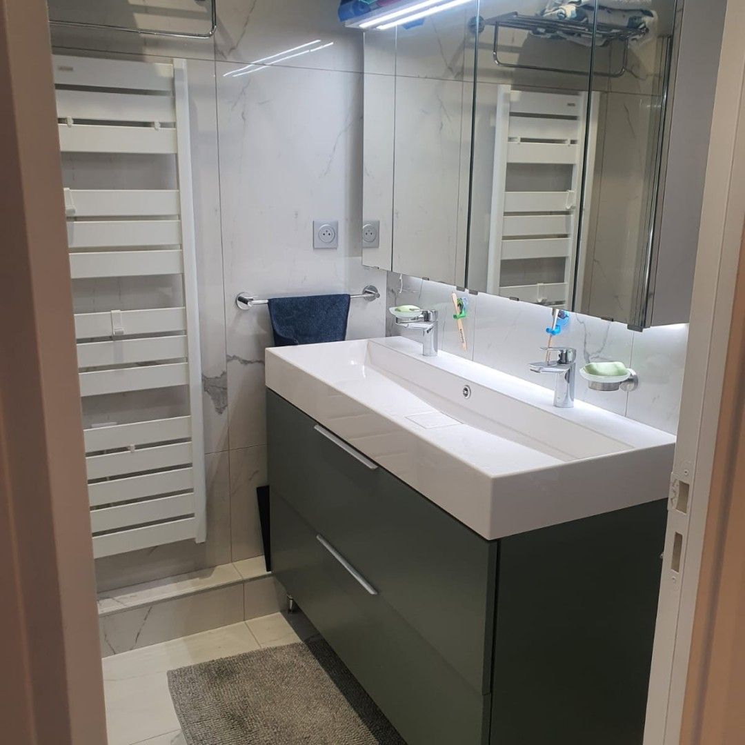 Salle de bains avec miroir éclairé et meuble blanc et noir.