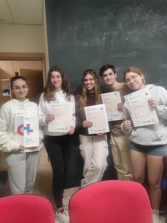 Un grupo de jóvenes están de pie uno al lado del otro sosteniendo papeles frente a una pizarra.