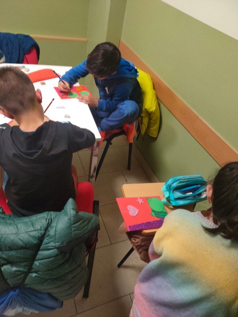Un grupo de niños están sentados alrededor de una mesa haciendo manualidades.