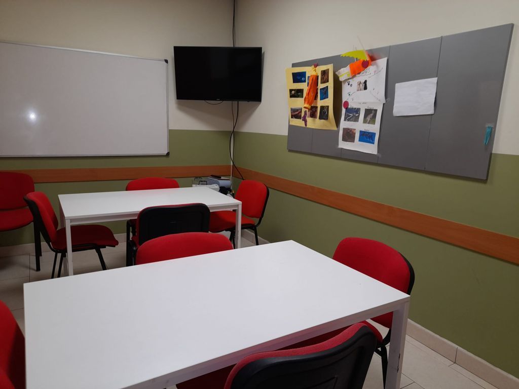 Un aula con mesas y sillas y un televisor en la pared.