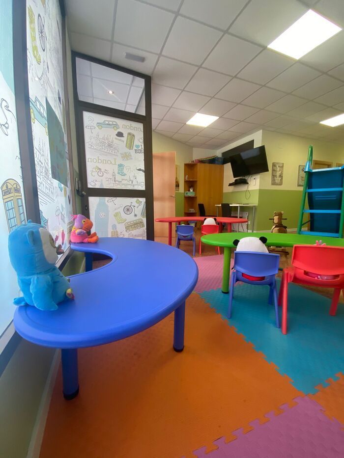 Una habitación con mesas y sillas y una mesa azul con un animal de peluche encima.