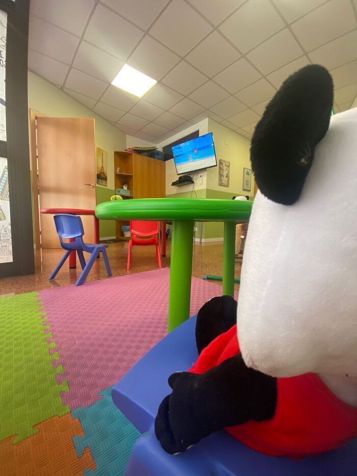 Un oso panda de peluche está sentado en una silla azul en una sala de juegos.