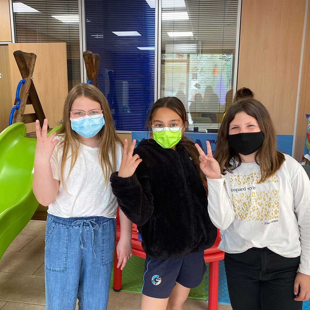 Tres chicas jóvenes con mascarillas posan para una fotografía.