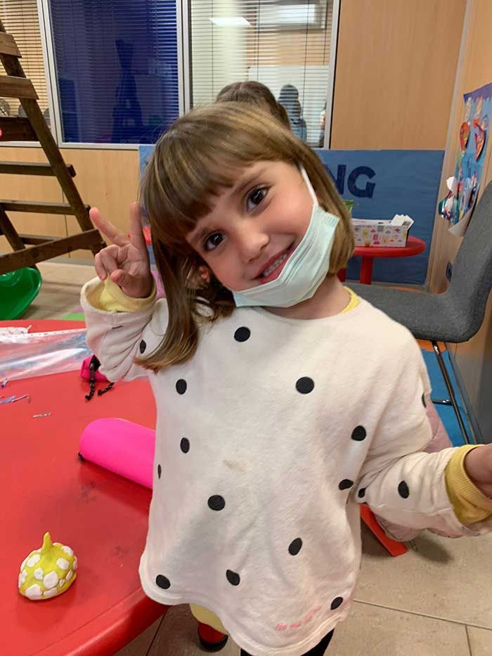 Una niña que lleva una mascarilla está haciendo un signo de paz.