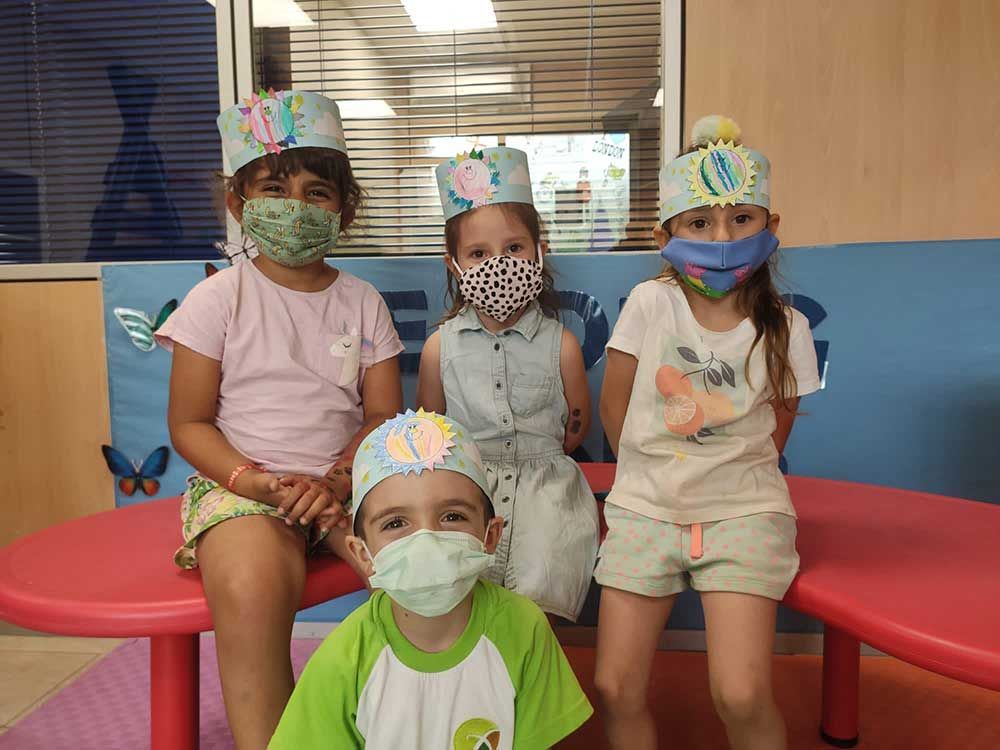 Un grupo de niños con mascarillas y sombreros están sentados en un banco.