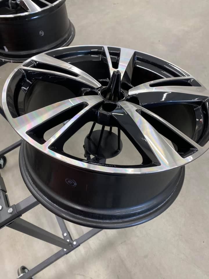 Une jante de voiture en alliage noir et argent, montée sur un support dans un atelier.