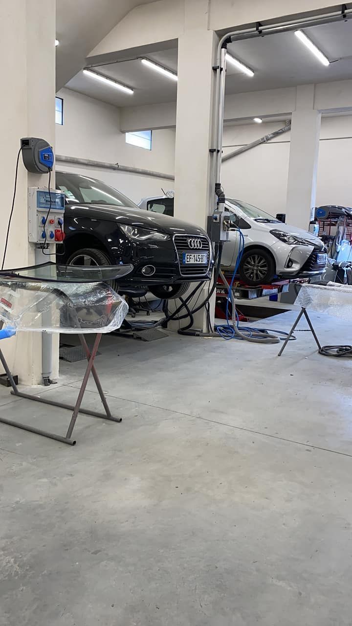 Deux voitures surélevées sur des ponts élévateurs à l'intérieur d'un atelier de réparation automobile.