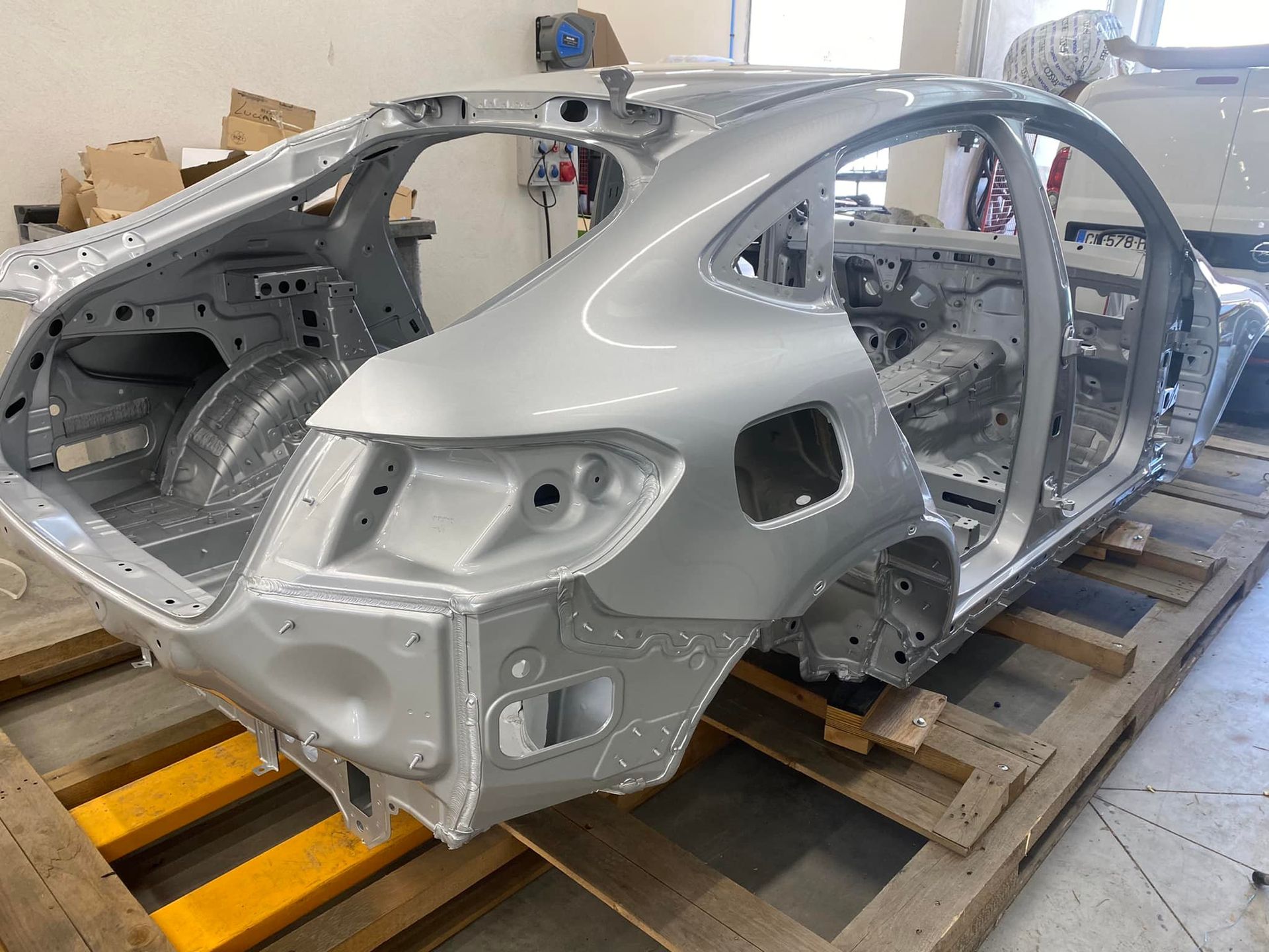 Châssis de voiture argenté monté sur une palette en bois à l'intérieur d'un atelier.