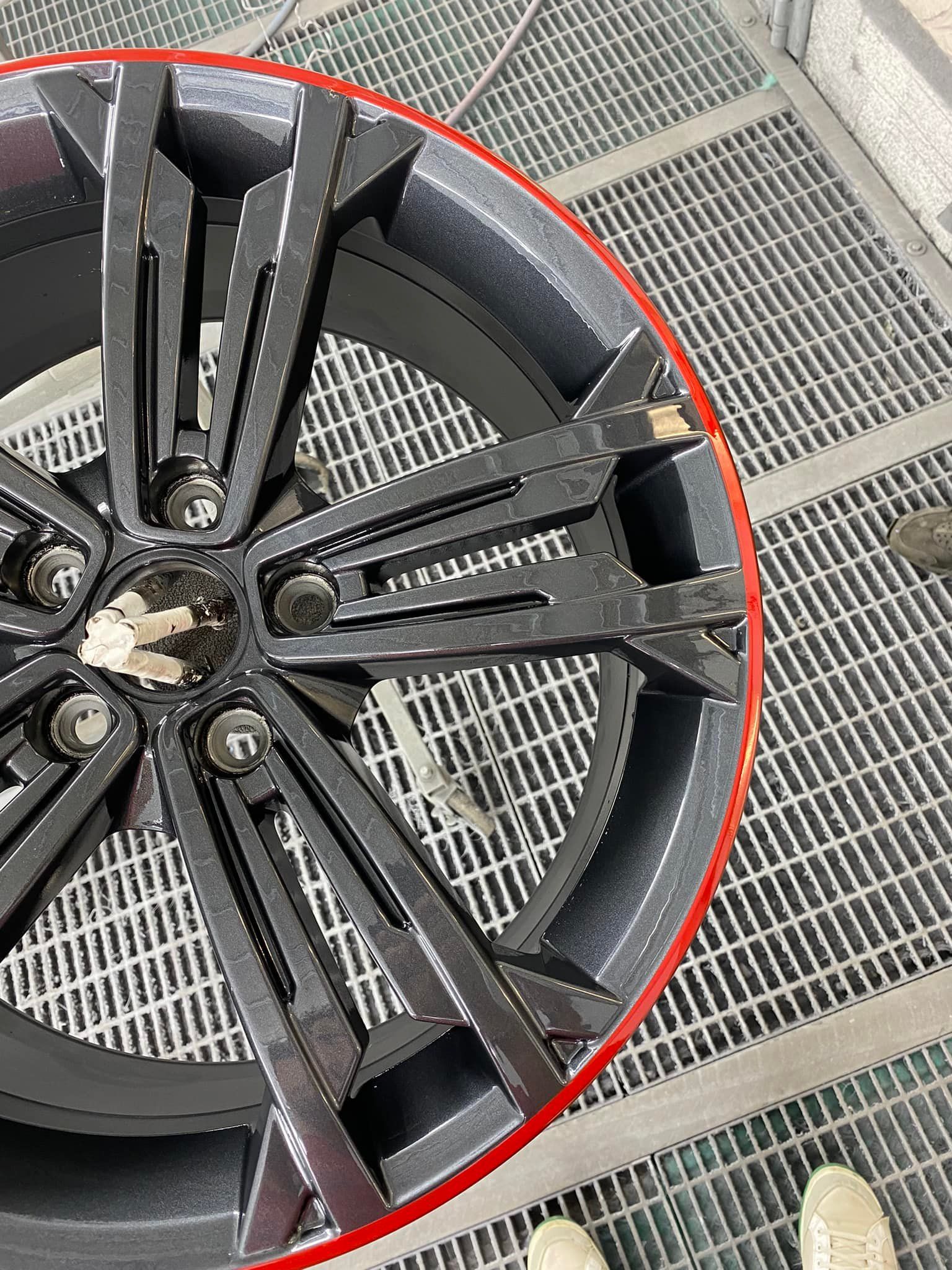 Une roue de voiture gris foncé avec un liséré rouge posée sur un sol en grille métallique.