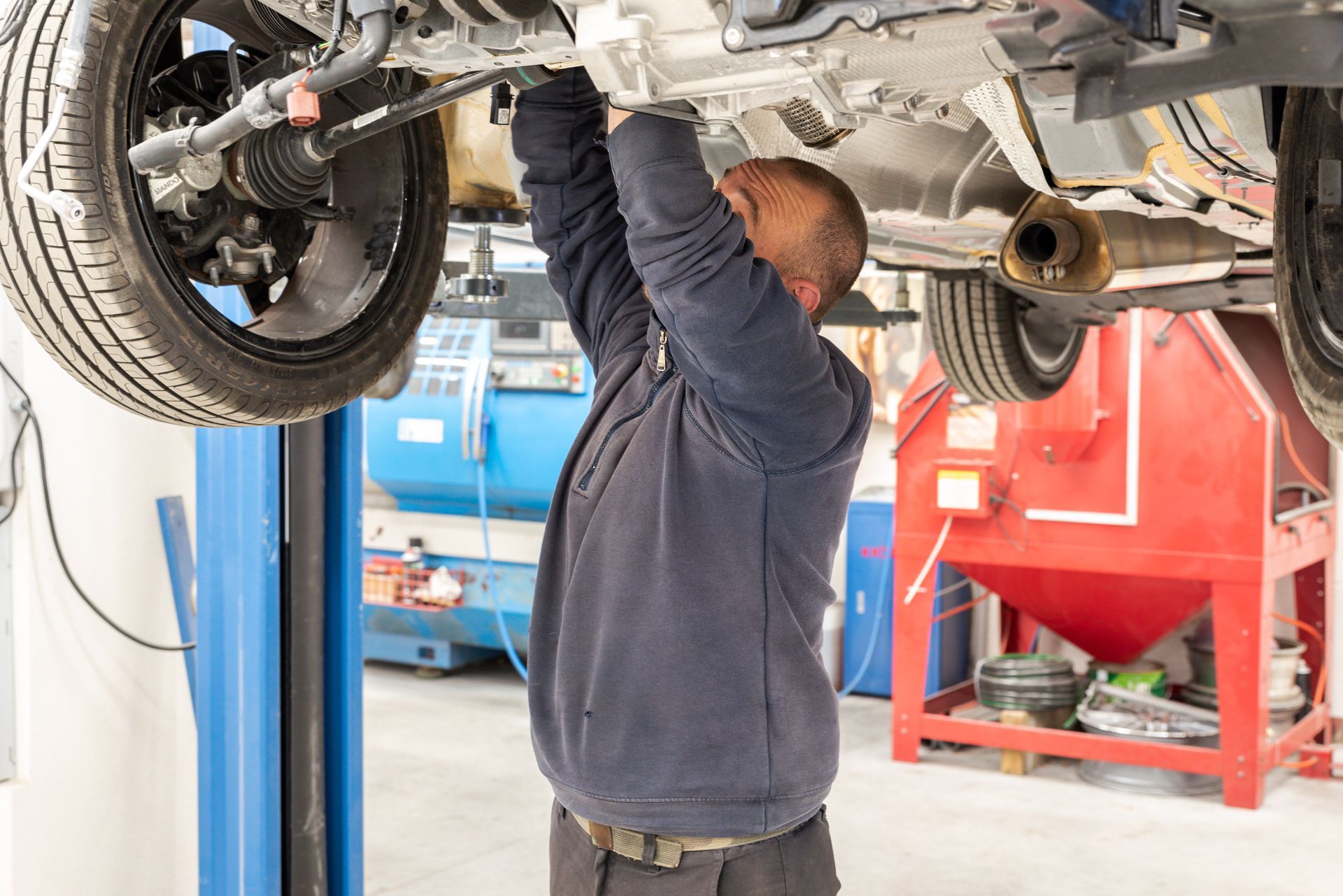 Un mécanicien travaille sous une voiture soulevée par un pont élévateur dans un atelier.