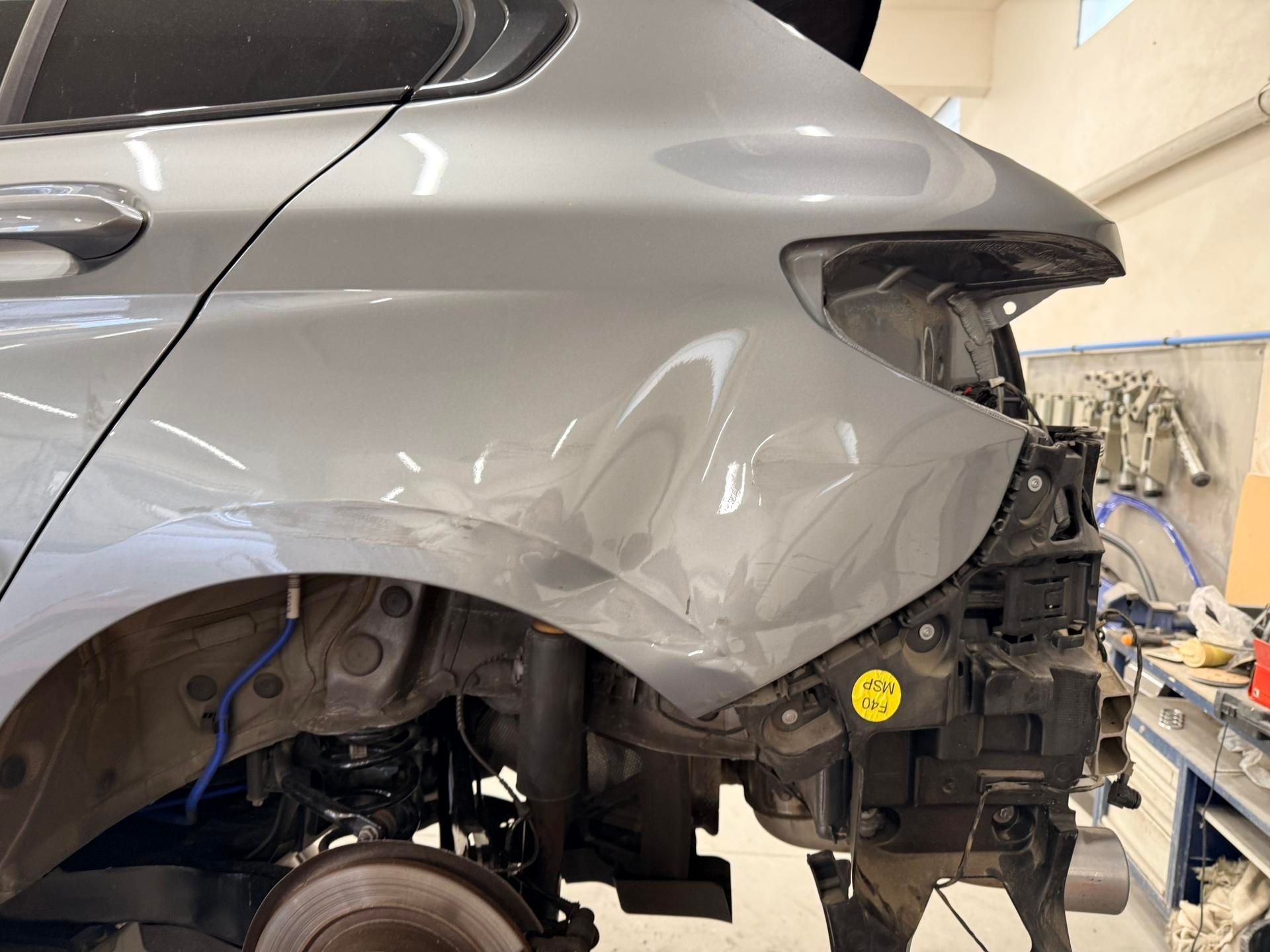 Panneau latéral arrière d'un véhicule gris dans un atelier de réparation, montrant un enfoncement au-dessus de la roue.