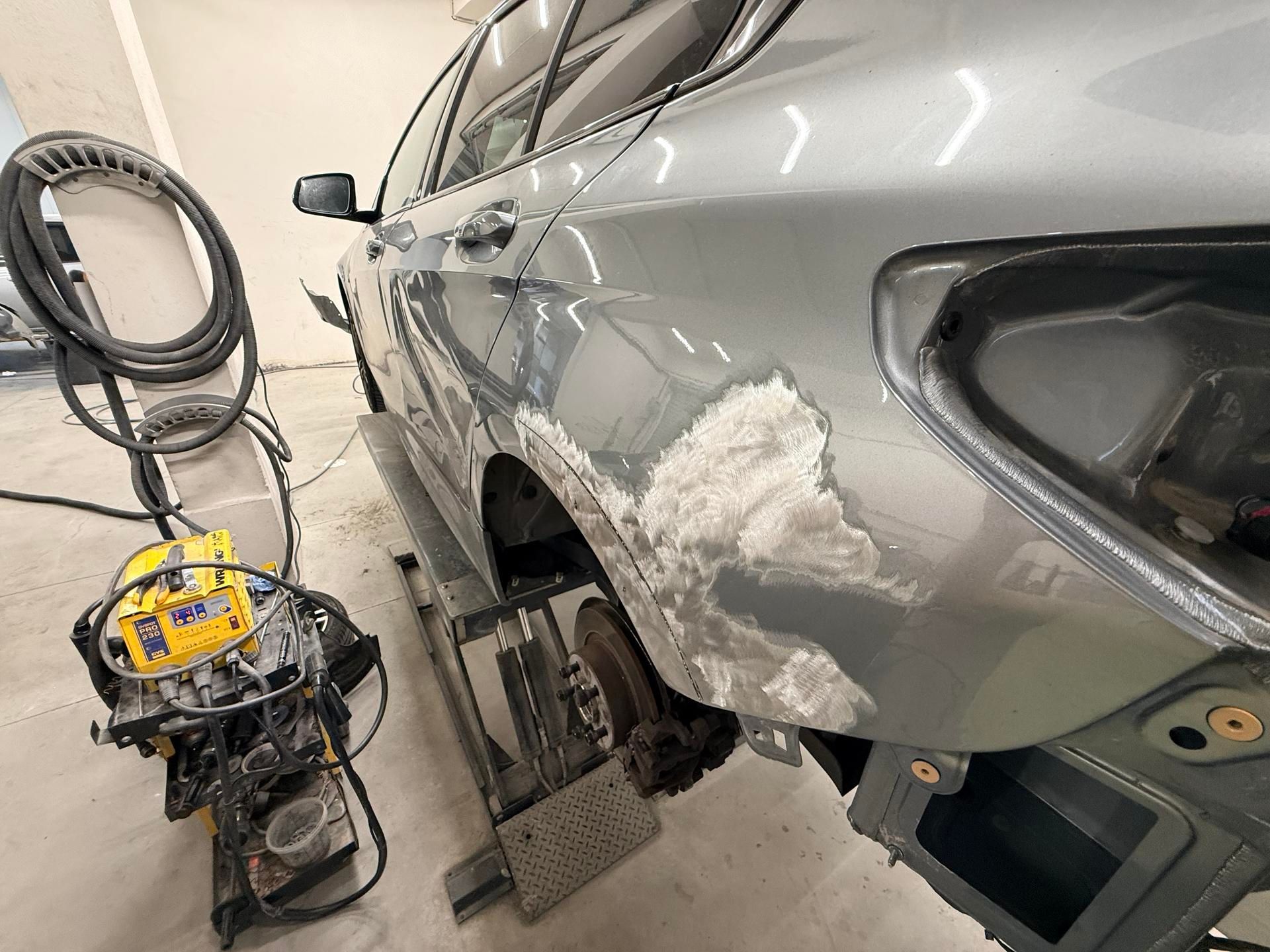 Un véhicule argenté sur un pont élévateur, avec une grande zone poncée sur le panneau arrière.