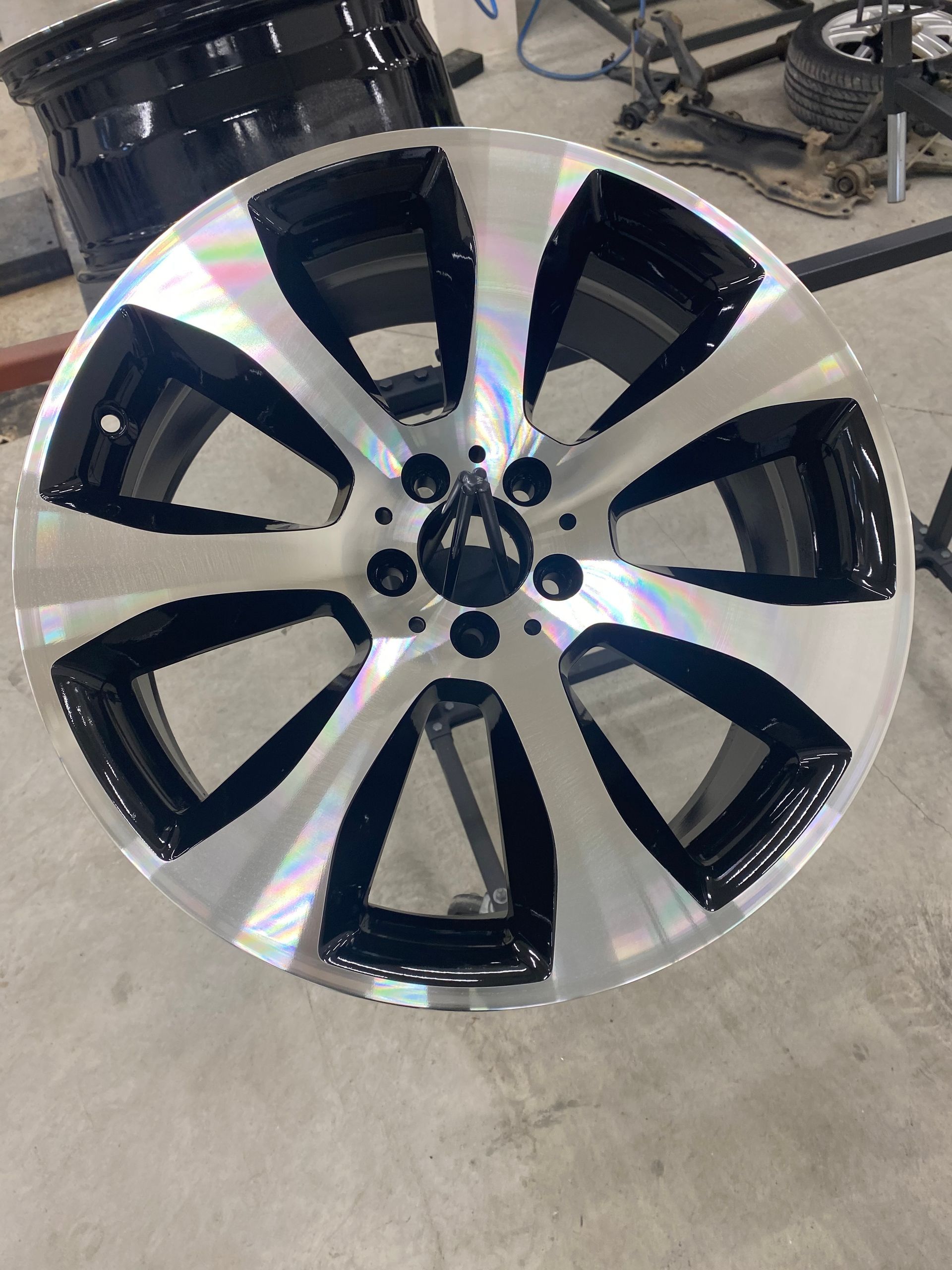 Une jante de voiture en alliage à cinq branches, finition usinée noire et argentée, placée dans un garage.