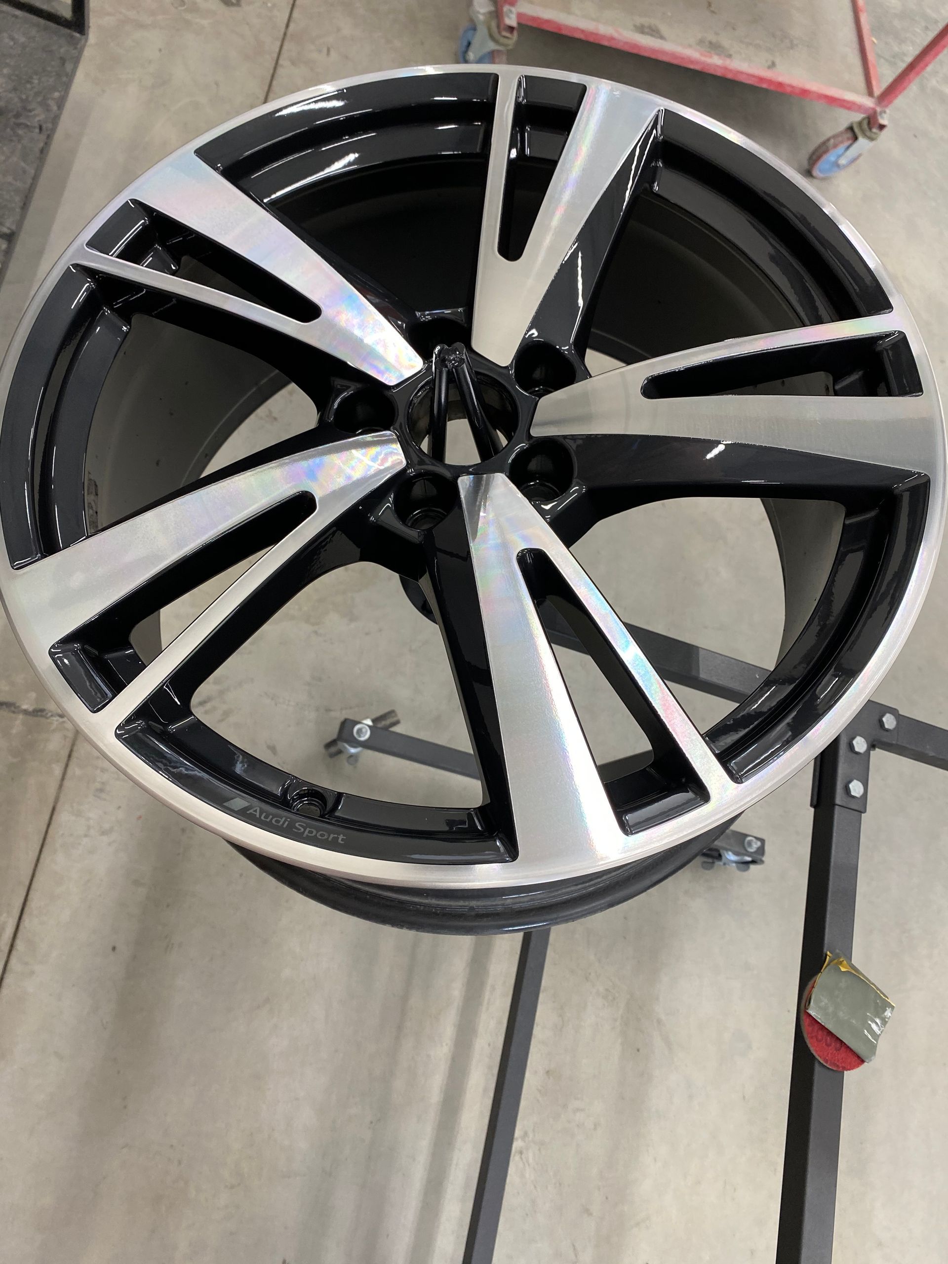 Une jante de voiture en alliage noir et argent à cinq branches, posée sur un support d'atelier.