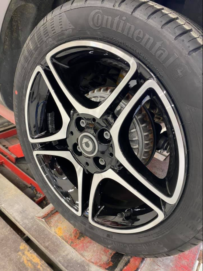 Gros plan sur une jante de voiture en alliage noir et argent à cinq branches, équipée d'un pneu Continental.