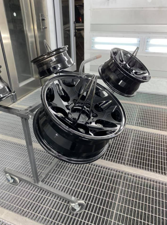 Trois jantes de voiture noires brillantes montées sur un support métallique.