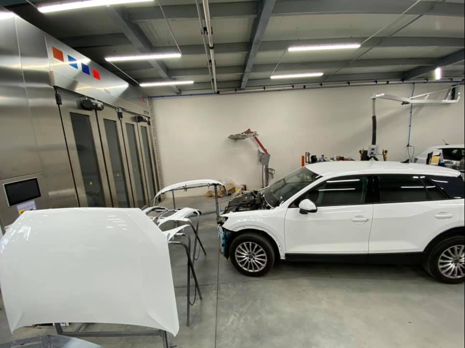 Une voiture blanche et son capot démonté à l'intérieur d'un atelier de carrosserie.