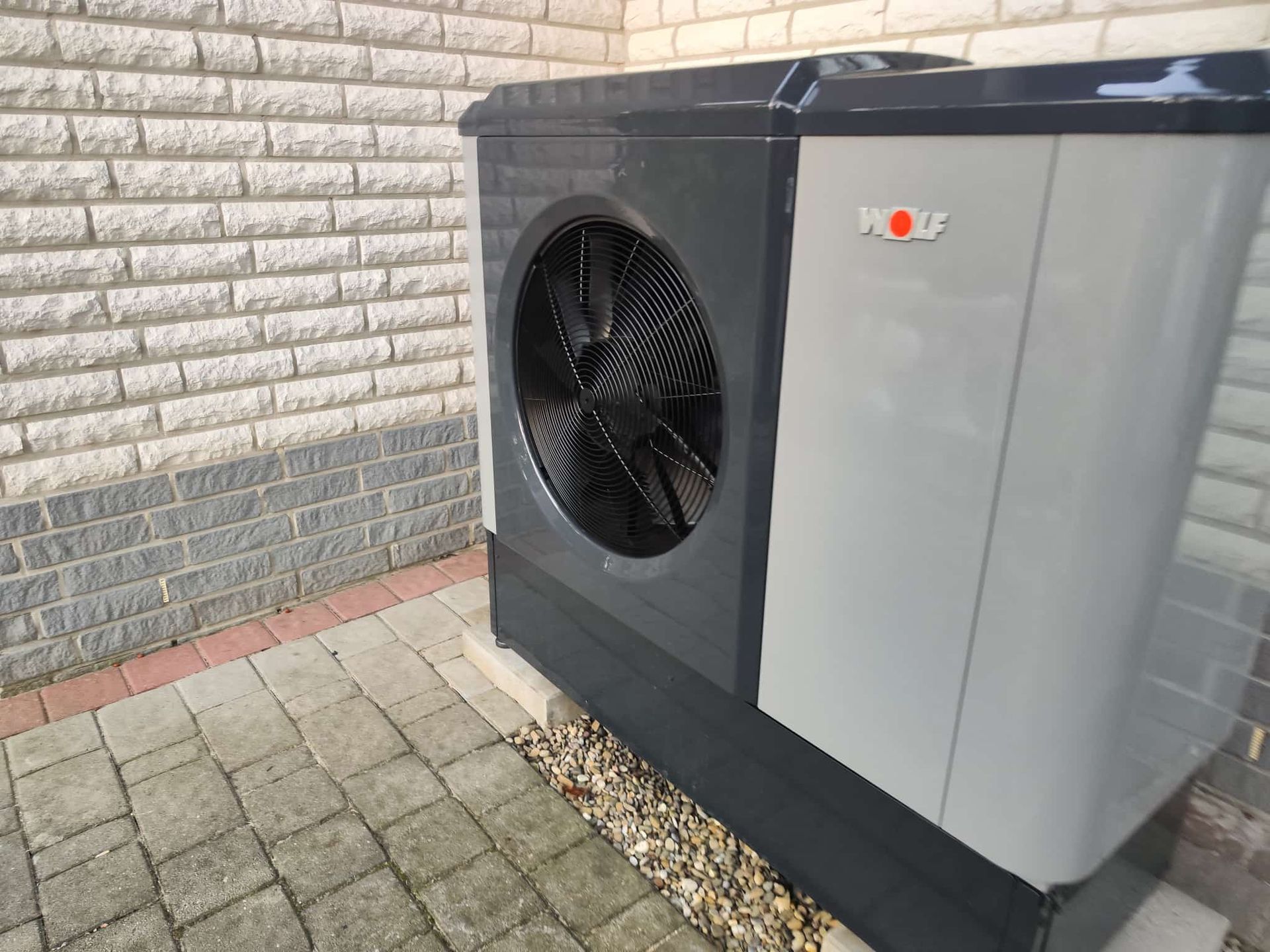 Neben einer Backsteinmauer steht eine schwarz-graue Klimaanlage.