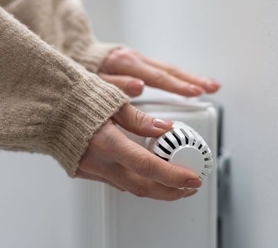 Eine Person stellt einen Thermostat an einem Heizkörper ein.