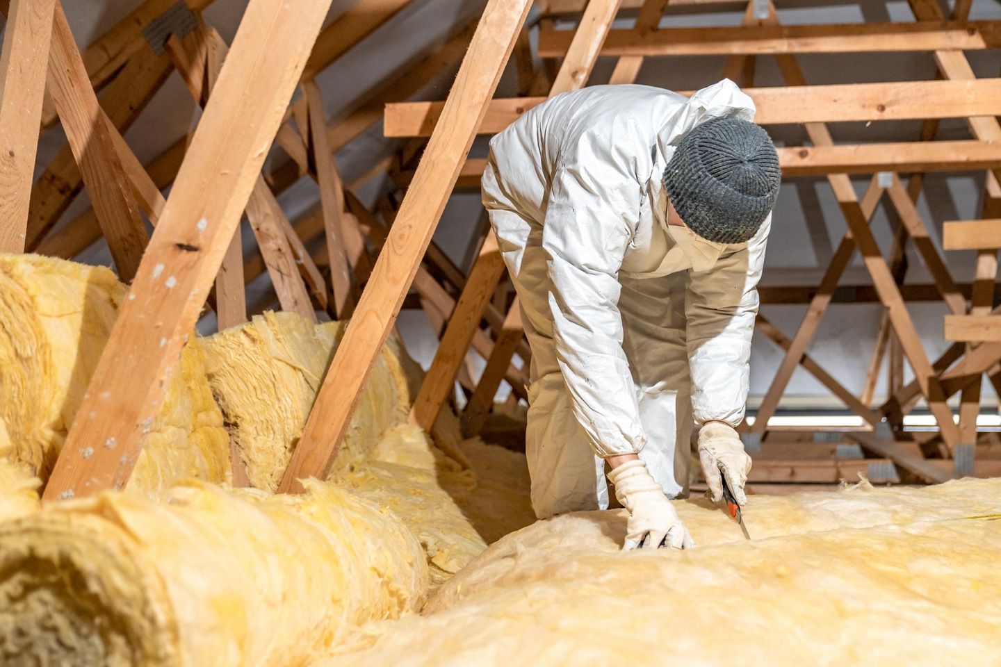 Ouvrier en combinaison de protection installant de l'isolant dans un grenier.
