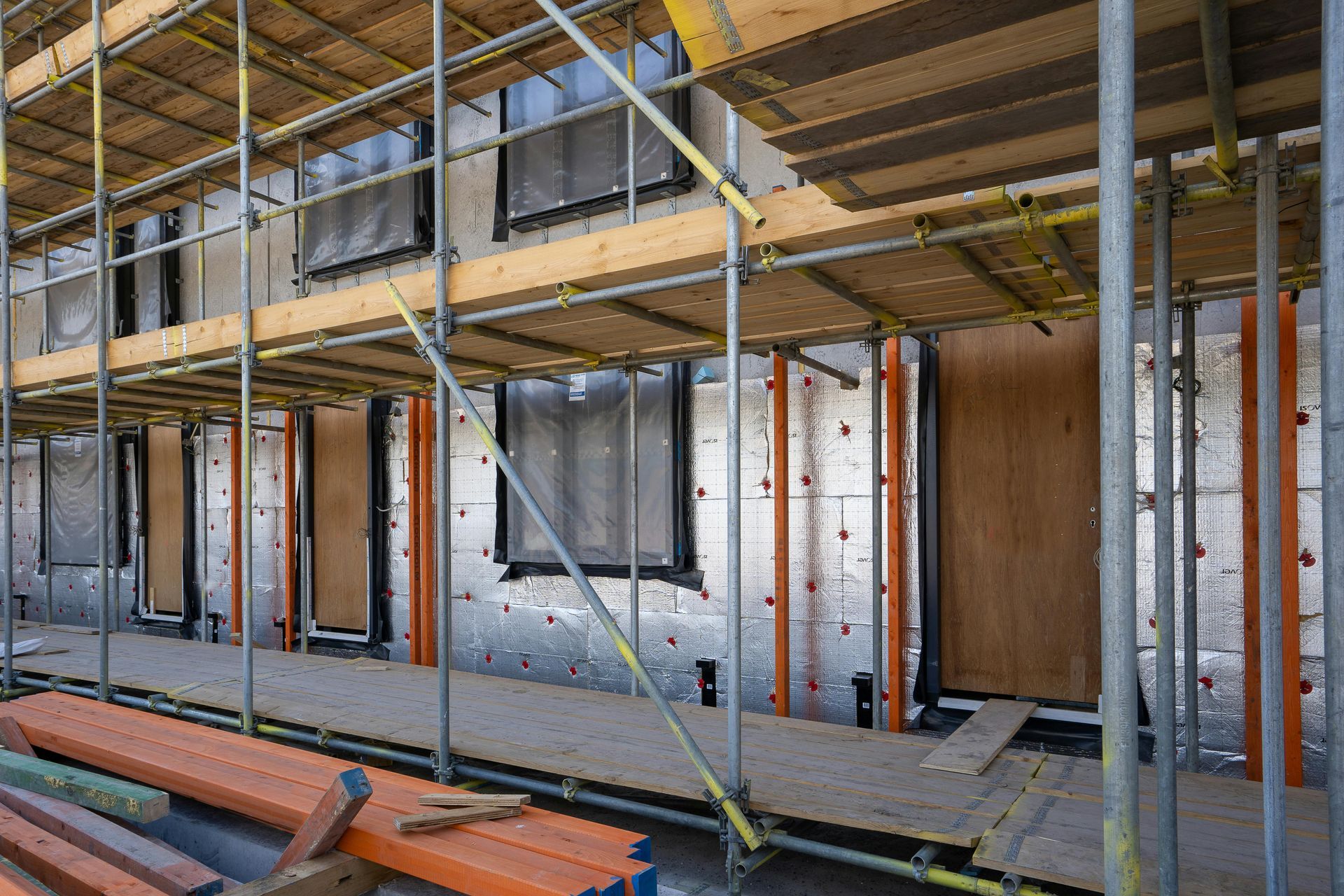 Bâtiment en construction avec échafaudages, charpente métallique, contreplaqué et murs apparents.