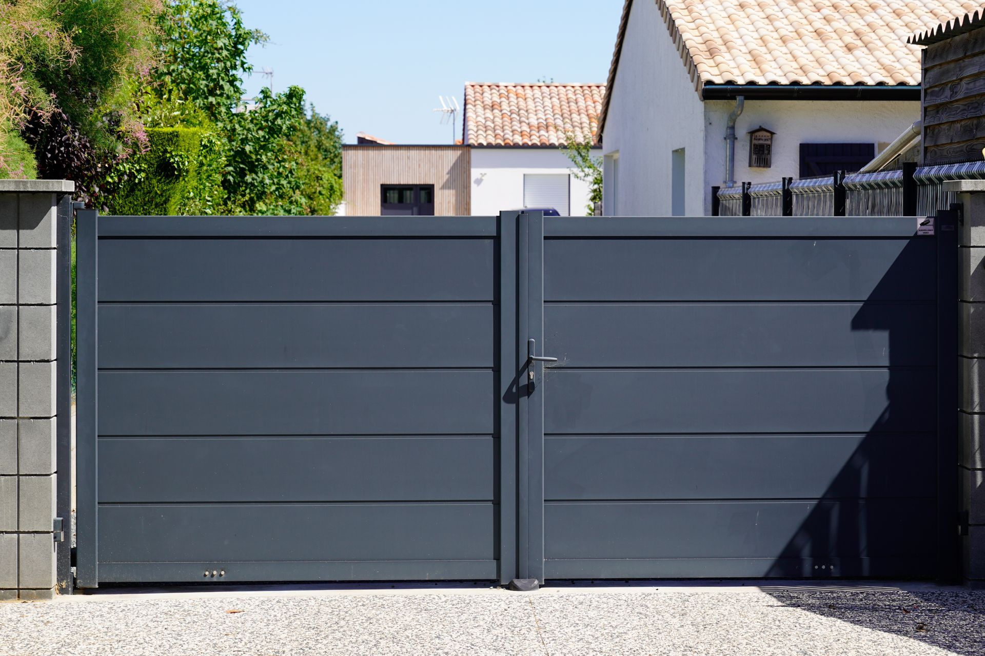 Portail double gris foncé devant une maison.