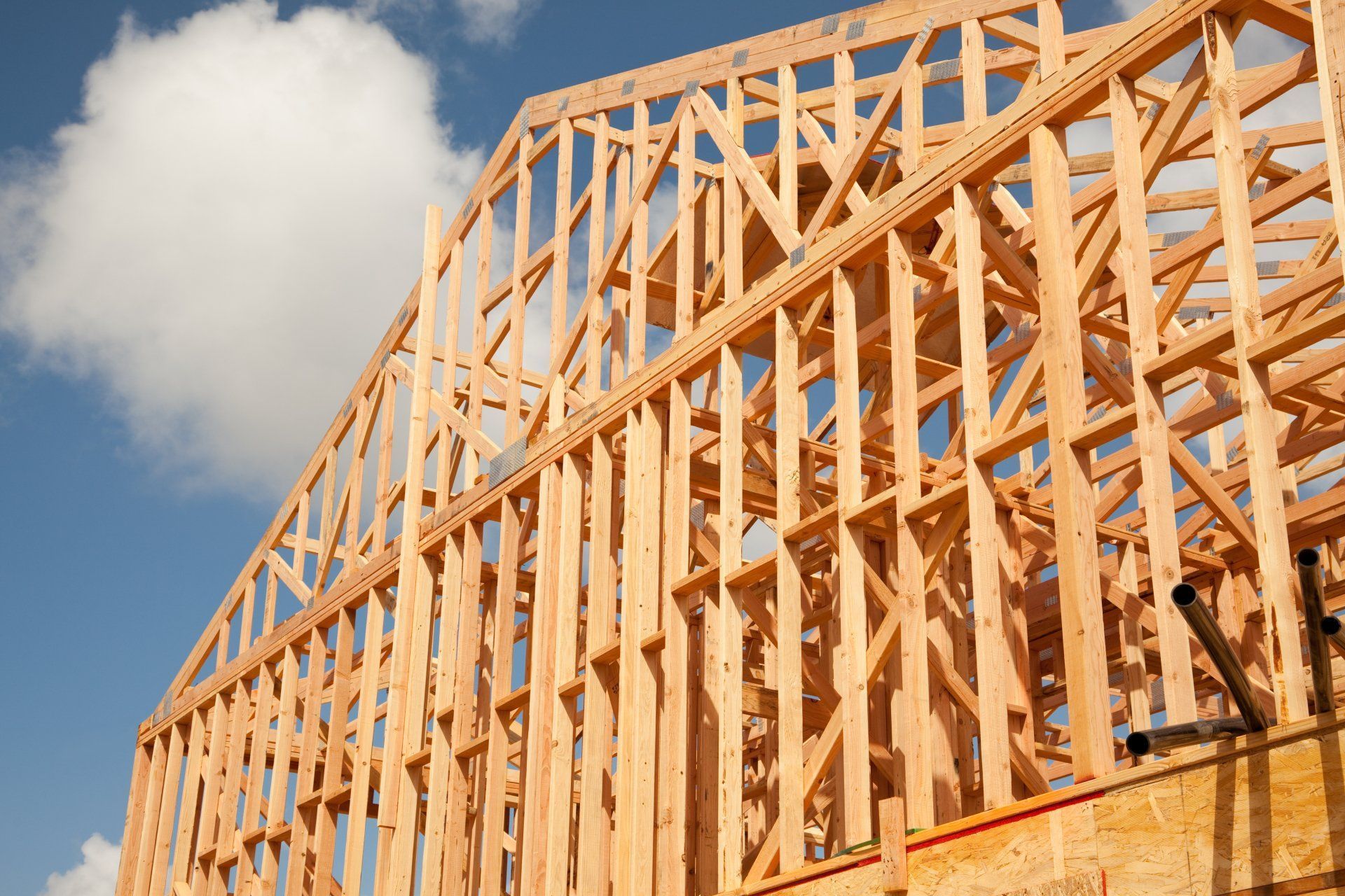 La charpente en bois d'une maison en construction se détache sur un ciel bleu nuageux.
