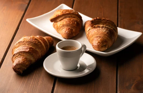 Zwei Tassen Latte-Art-Kaffee auf Untertassen, eine davon mit Löffel, auf einem hellen Tisch