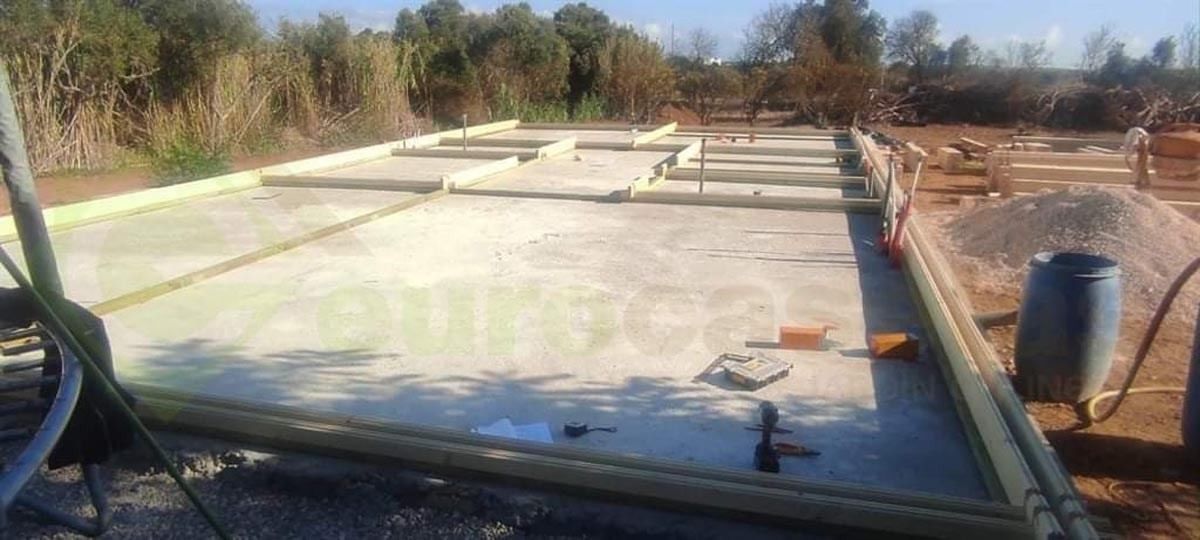 Se está construyendo un piso de concreto en un campo con árboles al fondo.