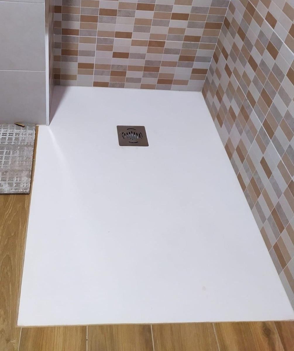 Una cabina de ducha blanca con desagüe cuadrado en un baño.