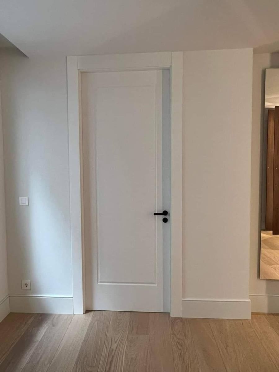 Una puerta blanca con manija negra está en una habitación con pisos de madera.