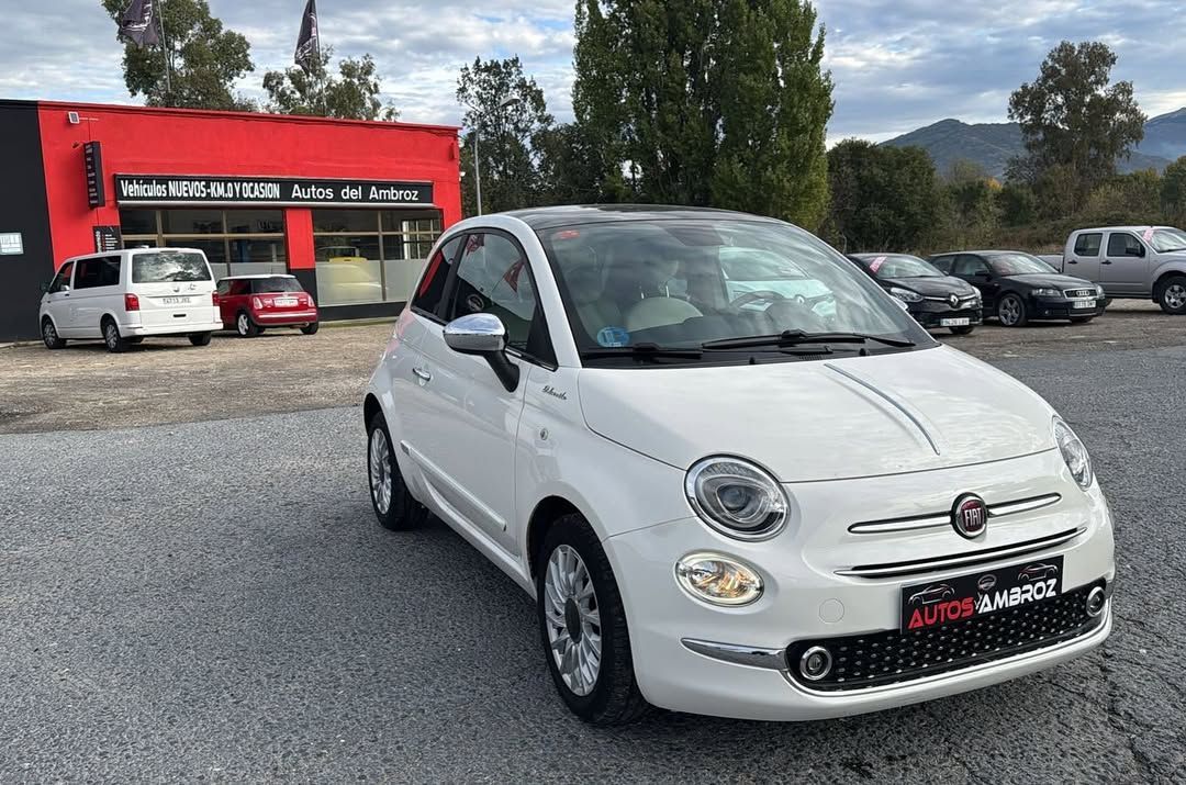 Coches aparcados frente a un edificio rojo con detalles negros. Un árbol a la derecha.