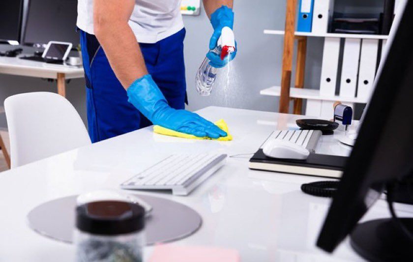 Un hombre está limpiando un escritorio con una esponja y una botella de spray.