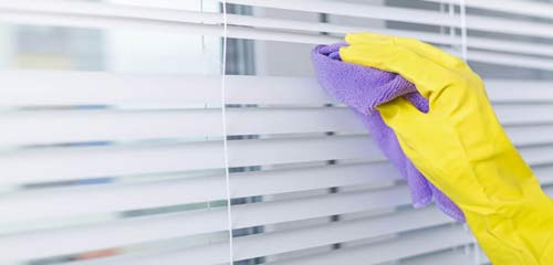 Una persona que lleva guantes amarillos está limpiando persianas con un paño morado.