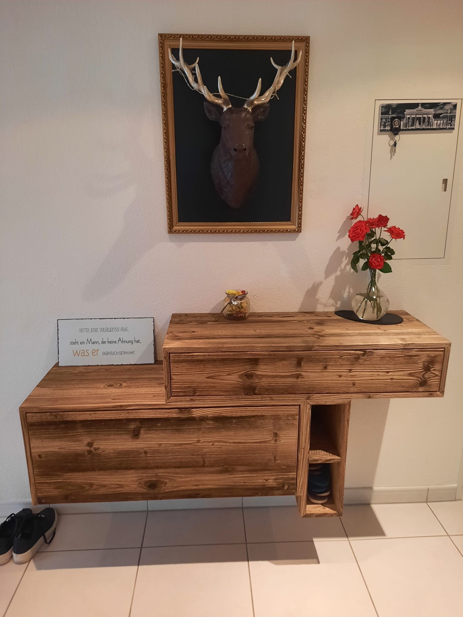 Eine Holzkommode mit einem Hirschbild an der Wand darüber.