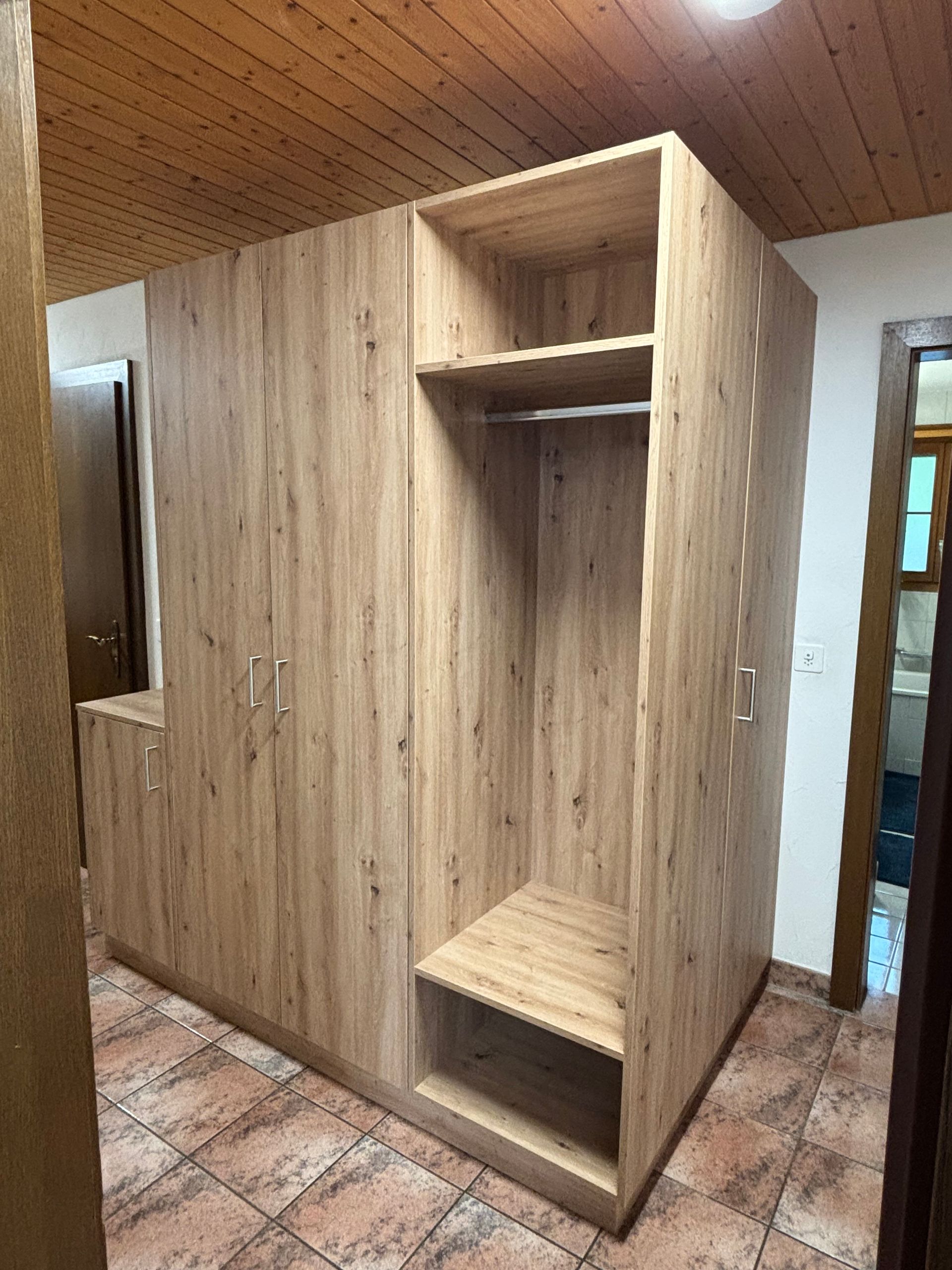 Ein grosser Holzkleiderschrank steht in einem Flur neben einem gefliesten Boden.