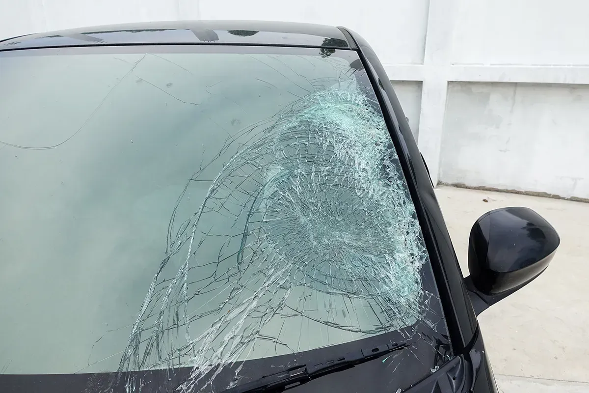 Ein schwarzes Auto mit kaputter Windschutzscheibe steht am Straßenrand.